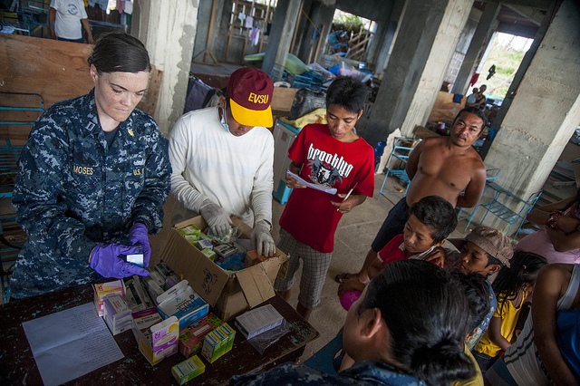 A man looks on as a Navy physician assistant assists Philippine nurses in treating patients.